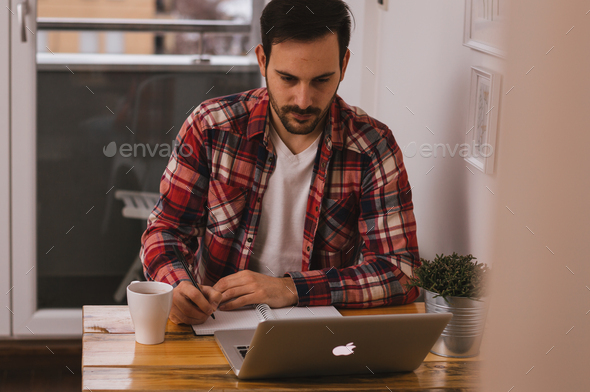 Focused man working from the home office, writing something in his notebook. - Stock Photo - Images