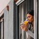 A girl standing by the window, using a phone, drinking orange juice. - PhotoDune Item for Sale