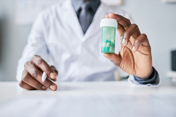 Close up black doctor holding bottle of pills to camera - Stock Photo - Images