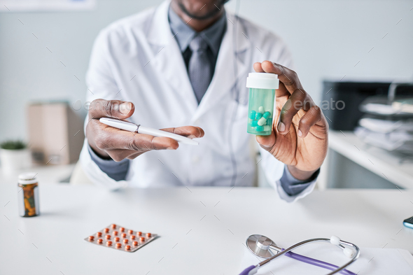Close up African American doctor holding bottle of pills to camera pointing - Stock Photo - Images