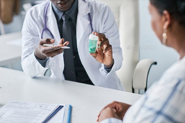 Close up black doctor holding bottle of pills consulting patient in clinic - Stock Photo - Images