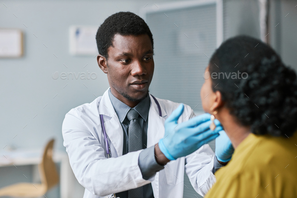 Young black doctor consulting patient in clinic doing throat exam with palpation