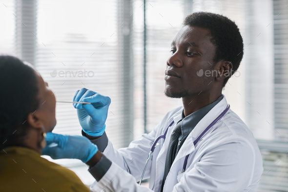 Young black doctor consulting patient in clinic doing throat exam for flu