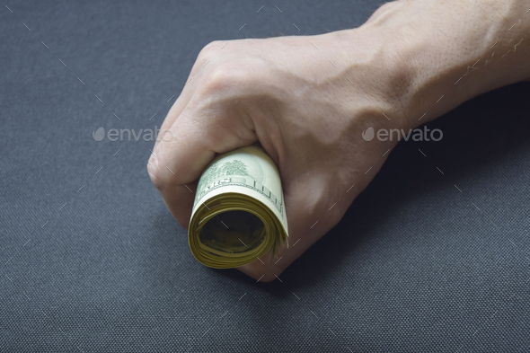 Bundle of rolled up dollar bills clutched in caucasian man\'s hand. Male holding cash money currency