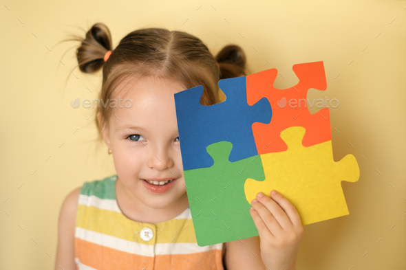 Kid cheerfully while closing eye holding puzzle of colorful details in hand - Stock Photo - Images