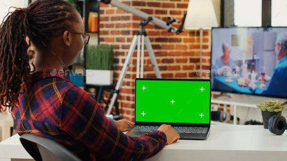 Female employee looking at greenscreen display on laptop - Stock Photo - Images