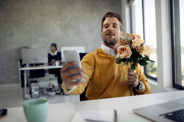 Mid adult businesswoman holding bouquet of flowers while having video call in the office.