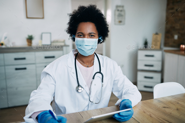 African American doctor wearing face mask while working on touchpad in her office.