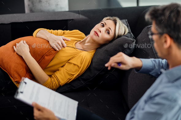 Mid adult woman listening to her therapist while lying down on the psychiatrist\'s couch.