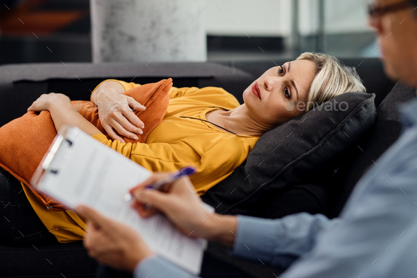 Thoughtful woman lying down on psychiatrist\'s couch during an appointment with her therapist.