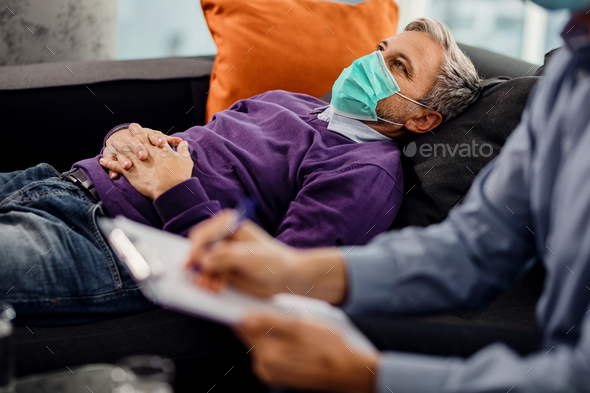 Pensive man wearing protective face mask while having counseling with his psychiatrist.