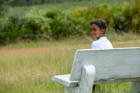 Portrait of boy seen sitting on bench in nature - Stock Photo - Images