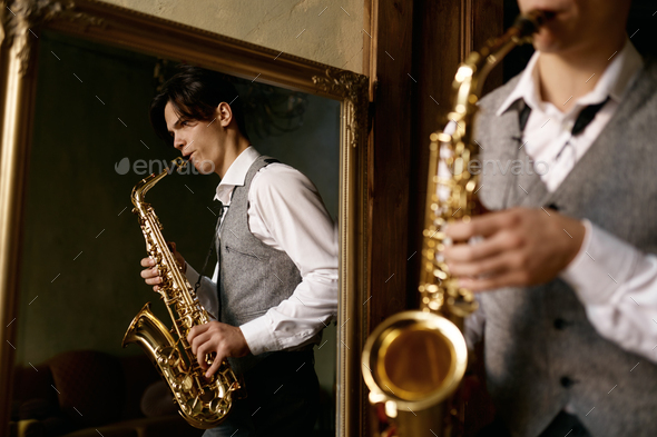 Young man playing saxophone in reflection of mirror at home - Stock Photo - Images