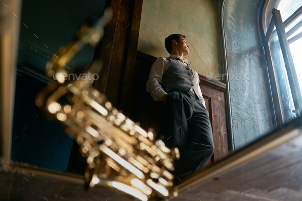 Pensive young saxophonist looking through window view from bottom - Stock Photo - Images