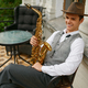 Smiling musician holding saxophone sitting on chair in balcony of his apartment - PhotoDune Item for Sale