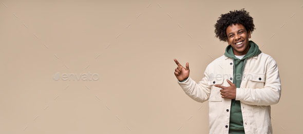 Happy African teenager pointing aside presenting, advertising isolated on beige. - Stock Photo - Images