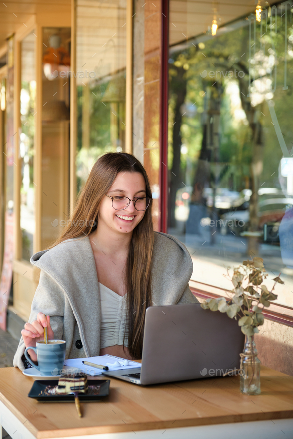 Smiling woman working with a notebook and a laptop in a coffee shop. - Stock Photo - Images
