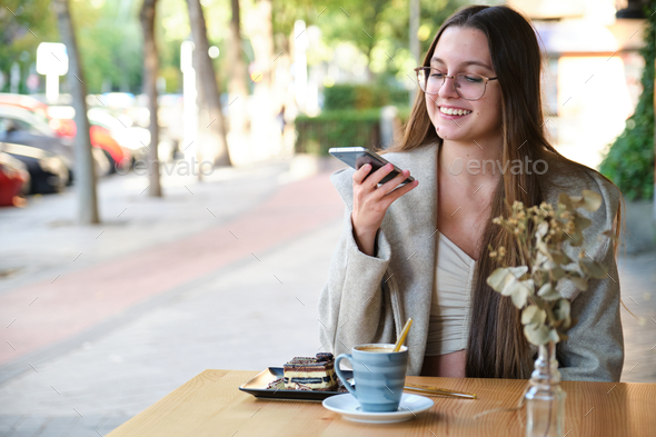 Smiling woman sending audio note with her phone in a coffee shop. - Stock Photo - Images