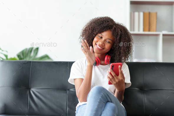 Beautiful young woman student sitting on sofa is video chatting on smartphone, smiling faces and ges - Stock Photo - Images