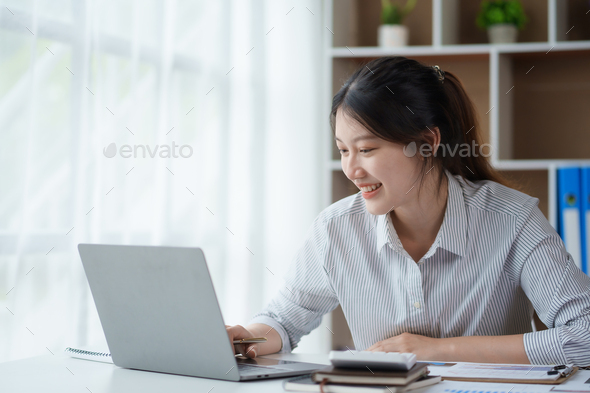 Bright and charming  young Asian woman working on her laptop with the intention of producing a satis - Stock Photo - Images