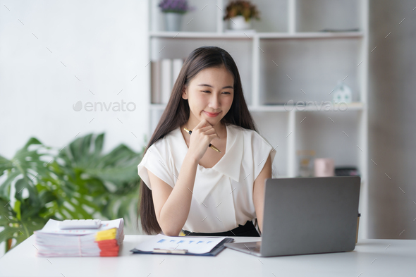 Beautiful Asian businesswoman working on laptop keyboard with document enjoying her work with smilin - Stock Photo - Images