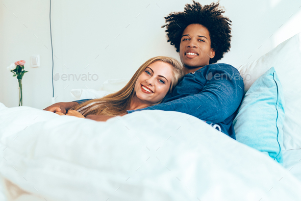 Young loving couple lying in bed cuddling looks each other under