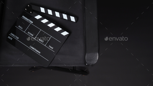 Clapperboard with director chair on black background.