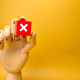Wooden hand holding red cube with error sign.Concept of negative decision making or choice of vote w - PhotoDune Item for Sale