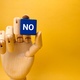 Wooden hand holding blue cube with the word NO on yellow background. Business concept. - PhotoDune Item for Sale