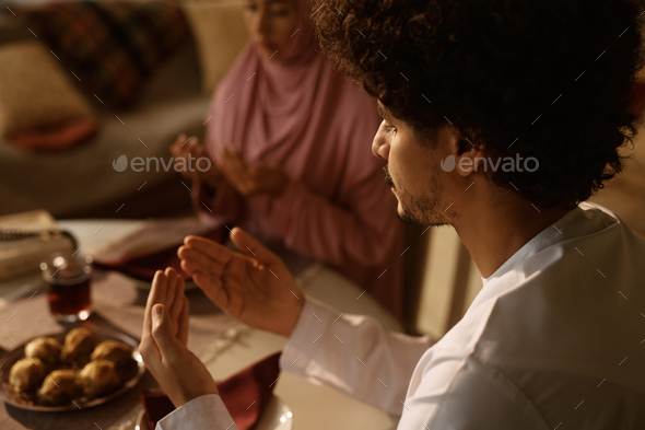Close up of religious Arab couple praying at dining table. - Stock Photo - Images