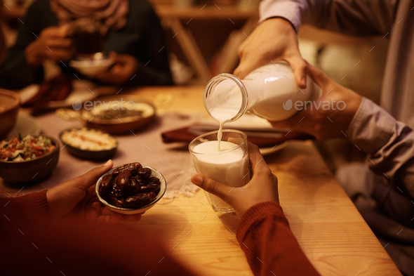 Close up of Muslim father pouring milk into daughter's glass during family meal at dining table. - Stock Photo - Images