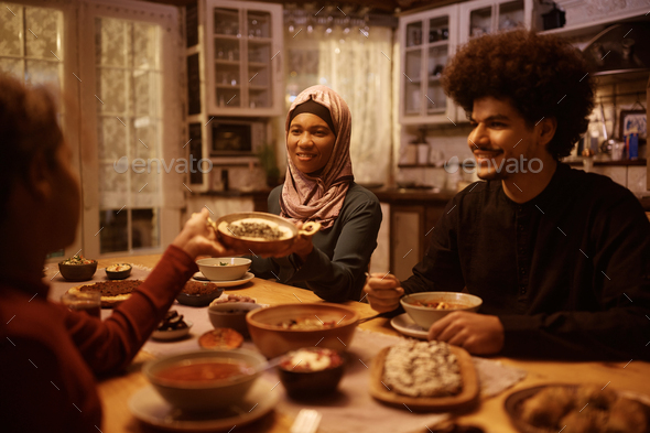 Happy Muslim woman passing food to her daughter during family dinner at dining table. - Stock Photo - Images