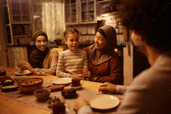 Happy Muslim multigeneration family talking during dinner at dining table. - Stock Photo - Images