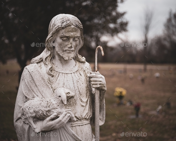 Weathered statue of Jesus Christ with a sheep in his hands on a blurred background