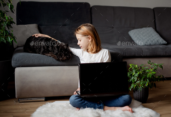 Portrait girl using laptop, sitting on the floor carpet with her dog in living room at home - Stock Photo - Images