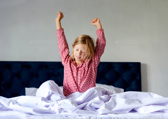 girl wearing pajama stretching hands after awakening, sitting in cozy bed - Stock Photo - Images