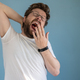 Bearded man in glasses and a white t-shirt yawns with mouth wide open, covering it with hand - PhotoDune Item for Sale