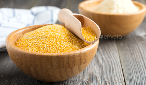 Raw corn grits polenta in a bamboo bowl on the old wooden background. Selective focus - Stock Photo - Images