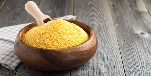 Raw corn grits polenta in a bamboo bowl on the old wooden background. Selective focus - Stock Photo - Images
