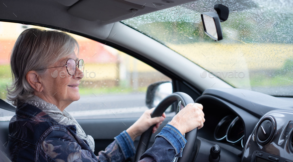Senior woman driver driving her car on a rainy day. Elderly woman holding the steering wheel