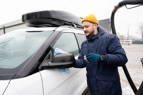 Man wipes american SUV car mirror with a microfiber cloth after washing in cold weather. - Stock Photo - Images