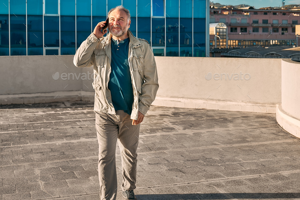 Portrait of middle aged bearded man having conversation on mobile phone near office building.  - Stock Photo - Images