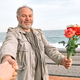 Smiling mature bearded man with colorful flowers holds and pulls hand leading her by the sea. - PhotoDune Item for Sale
