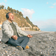 Bearded man sitting in lotus pose on pebble beach,meditating and listening music in headphones - PhotoDune Item for Sale