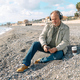 Happy middle-aged bearded man listening music in headphones while sitting on winter beach. - PhotoDune Item for Sale