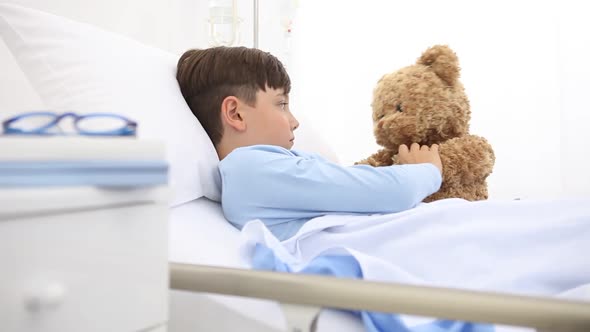 Child in hospital lying alone in bed play with teddy bear