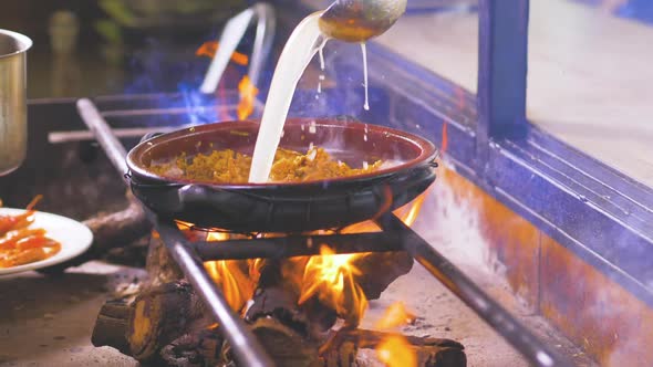 Hot sauce pouring from ladle on frying food on fire alt