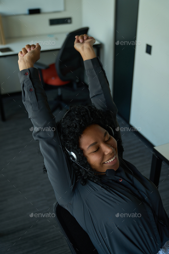 Smiling multiracial female with mobile headset stretching sweetly at workplace