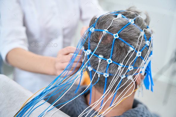 Patient in hospital gown sits with sensors on his head - Stock Photo - Images