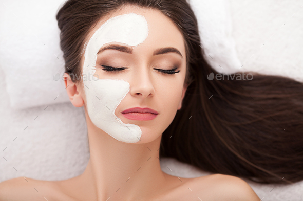 Attractive funny woman with a clay mask on her face Stock Photo by maksymiv